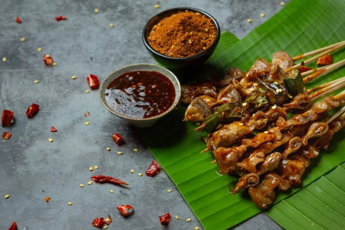 sate disajikan di atas daun pisang dengan saus pelengkap